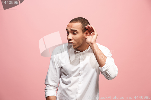 Image of The young man whispering a secret behind her hand over pink background