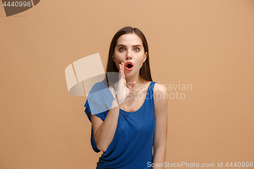 Image of The young woman whispering a secret behind her hand over paslel background