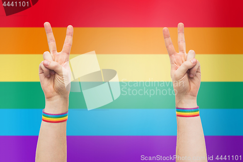 Image of hands with gay pride rainbow wristbands make peace