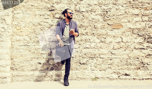 Image of man with smartphone at stone wall on city street