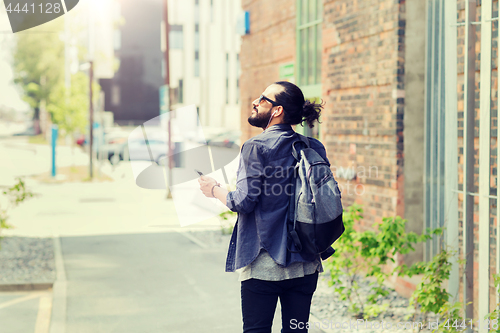 Image of man with earphones and smartphone walking in city