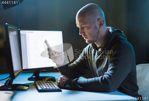 Image of hacker with smartphone and computers in dark room