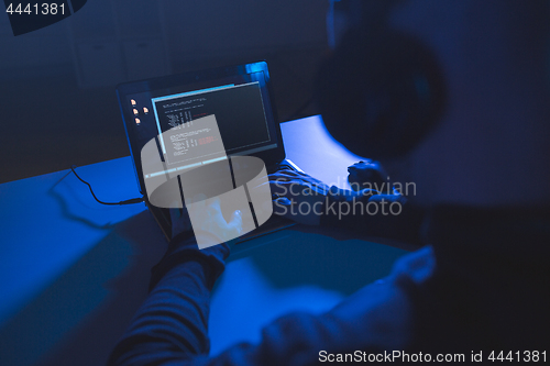 Image of hacker with coding on laptop computer in dark room