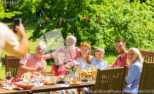 Image of happy family photographing at dinner in garden