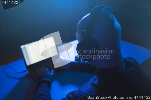 Image of hacker with headset typing on laptop in dark room