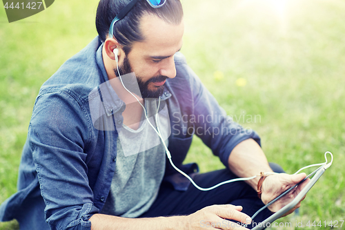 Image of man with earphones and tablet pc sitting on grass