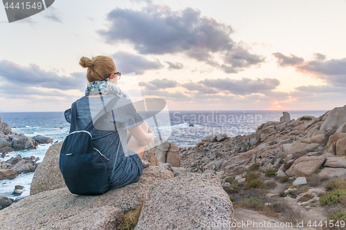 Image of Solo young female traveler watches a beautiful sunset on spectacular rocks of Capo Testa, Sardinia, Italy.