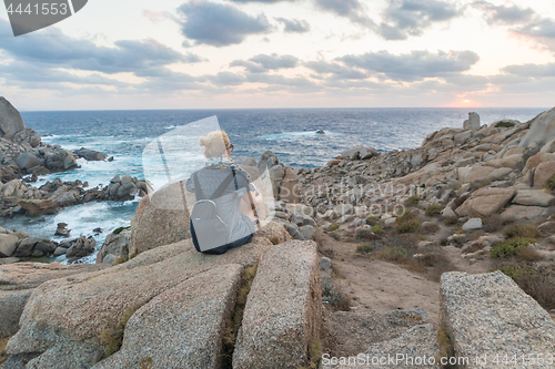 Image of Solo young female traveler watches a beautiful sunset on spectacular rocks of Capo Testa, Sardinia, Italy.