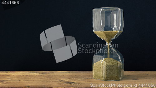 Image of a hourglass on a wooden underground with black background