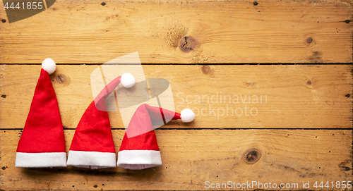 Image of three red Santa Claus hats with wooden background