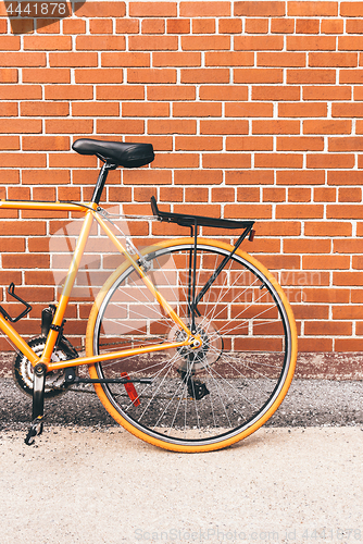 Image of Stylish orange bicycle near red brick wall