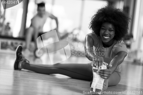 Image of woman in a gym stretching and warming up man in background worki