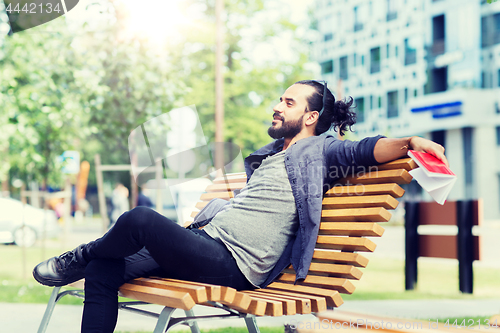 Image of man with notebook and bag on city street bench