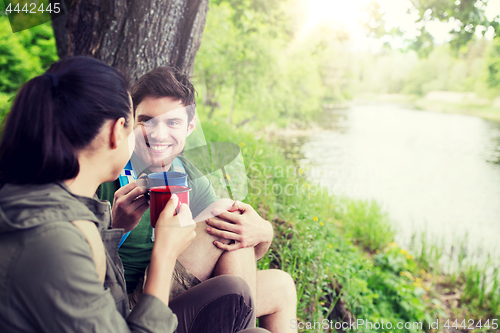 Image of happy couple with cups drinking in nature