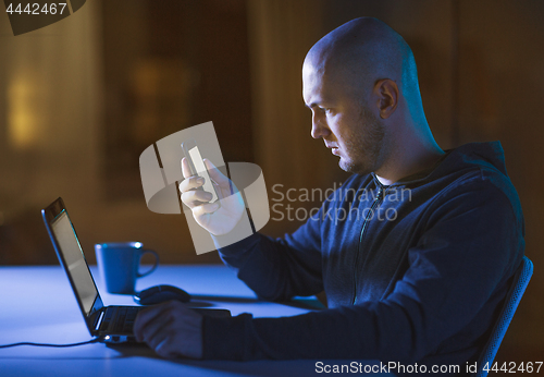 Image of hacker with laptop and smartphone in dark room