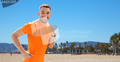 Image of smiling young man running at summer seaside