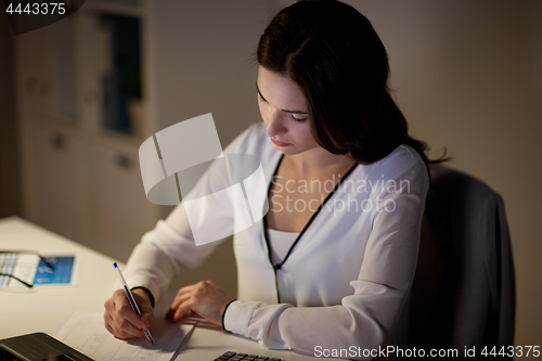 Image of woman with calculator and papers at night office