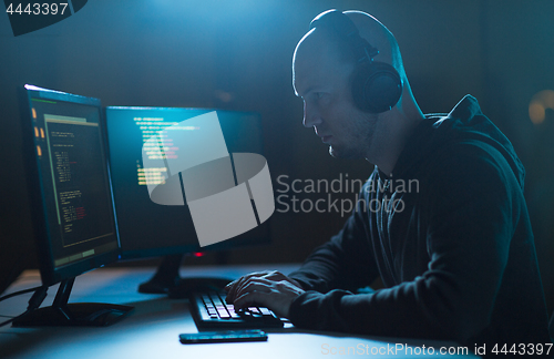 Image of hacker with coding on laptop computer in dark room