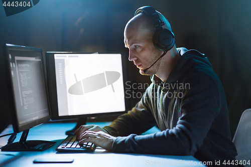 Image of hacker with computer and headset in dark room