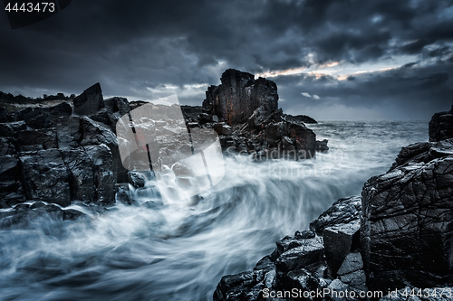 Image of Moody dramatic skies and large waves crash onto coastal rocks