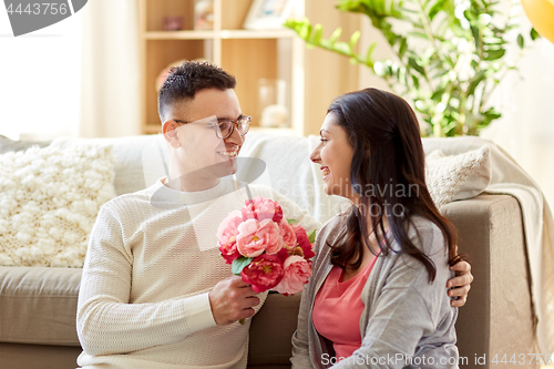 Image of happy husband giving flowers to his wife at home
