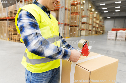 Image of warehouse worker packing parcel with scotch tape