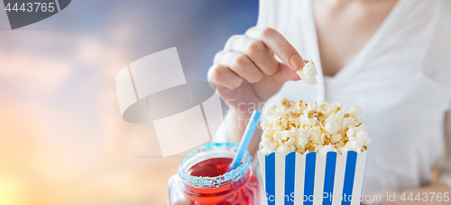 Image of woman eating popcorn with drink in glass mason jar