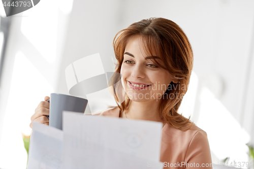 Image of businesswoman with papers drinks coffee at office