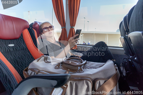 Image of Portrait of woman driving on moving bus sitting by window using mobile phone.