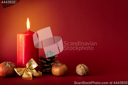 Image of Christmas decoration with a burning candle on red background