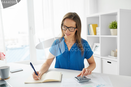 Image of happy woman with calculator and notebook at office