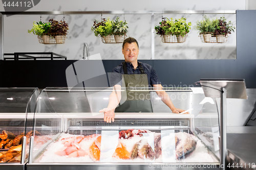 Image of male seller showing seafood at fish shop fridge