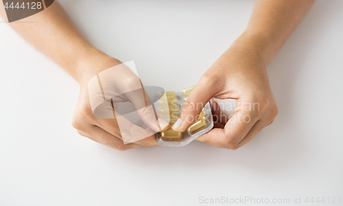 Image of woman hands opening pack of medicine capsules