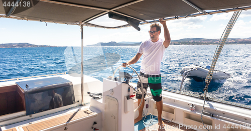 Image of Attractive male skipper navigating the fancy catamaran sailboat on sunny summer day on calm blue sea water.