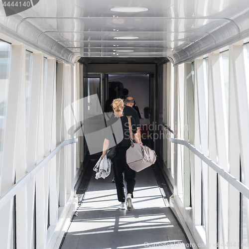 Image of Female passenger carrying the hand luggage bag, walking the airplane boarding corridor.