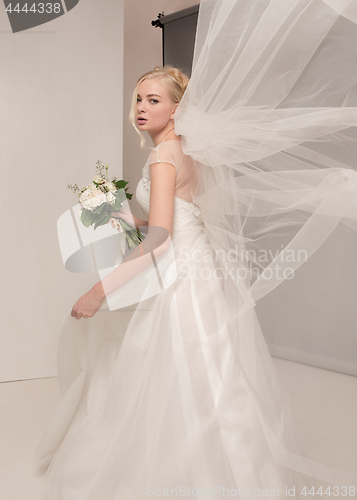 Image of Bride in beautiful dress standing indoors in white studio interior like at home. Trendy wedding style shot. Young attractive caucasian model like a bride tender looking.