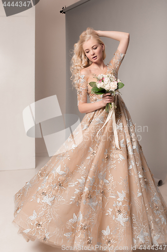 Image of Bride in beautiful dress standing indoors in white studio interior like at home. Trendy wedding style shot. Young attractive caucasian model like a bride tender looking.