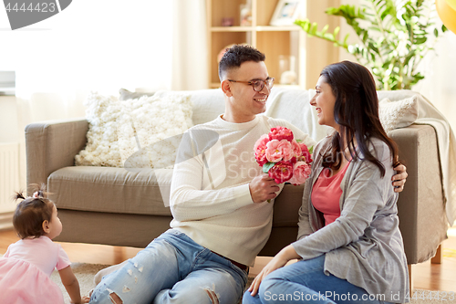 Image of happy husband giving flowers to his wife at home