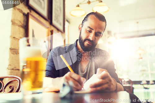 Image of man with beer writing to notebook at bar or pub