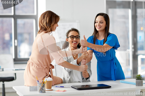 Image of group of businesswomen showing thumbs up at office
