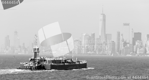 Image of Freight tug pushing cargo ship to the port in New York City and Lower Manhattan skyscarpers skyline in background.