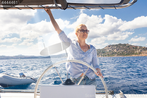 Image of Attractive blond female skipper navigating the fancy catamaran sailboat on sunny summer day on calm blue sea water.