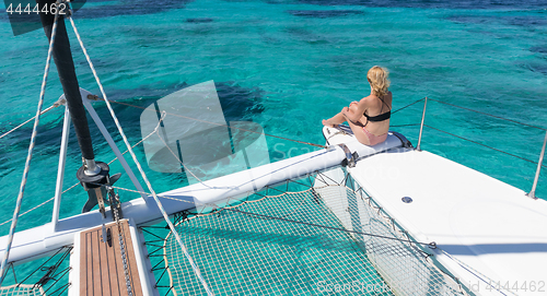 Image of Woman relaxing on a summer sailing cruise, sitting on a luxury catamaran in picture perfect turquoise blue lagoon near Spargi island in Maddalena Archipelago, Sardinia, Italy.