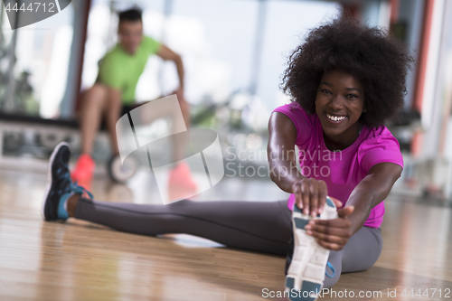 Image of woman in a gym stretching and warming up man in background worki