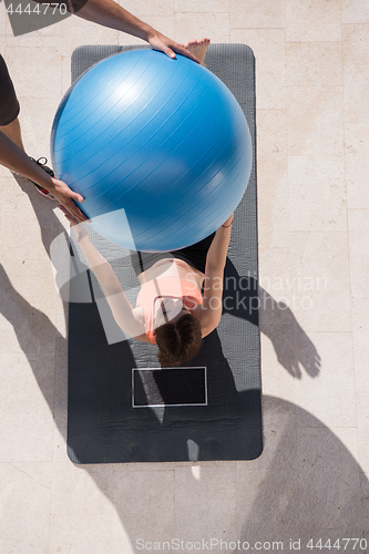 Image of woman and personal trainer doing exercise with pilates ball