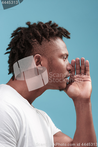 Image of The young Afro-American man whispering a secret behind her hand over blue background