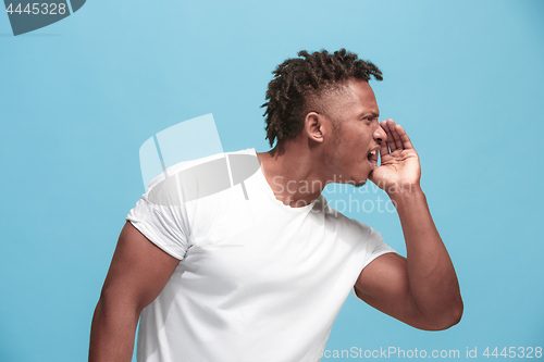 Image of The young afro-american man whispering a secret behind her hand over blue background