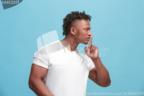 Image of The young afro-american man whispering a secret behind her hand over blue background