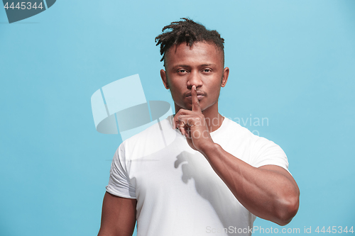 Image of The young afro-american man whispering a secret behind her hand over blue background