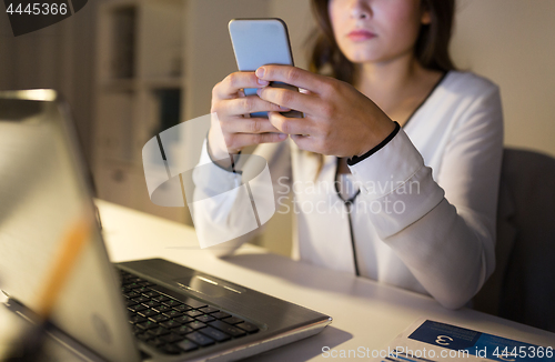 Image of businesswoman with smartphone and laptop at office